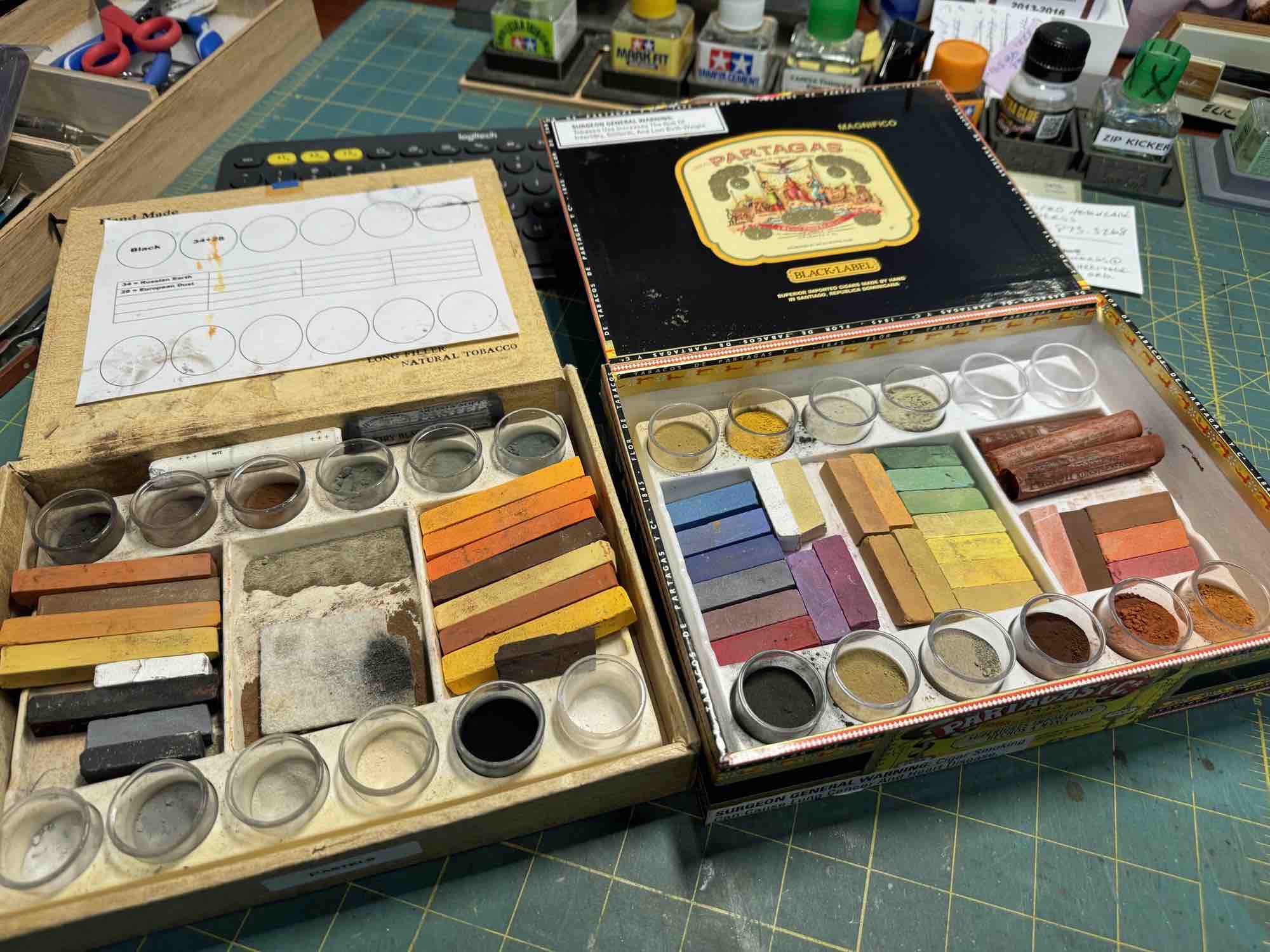 Pigments and pastel sticks organized in compartment trays stored inside cigar boxes.